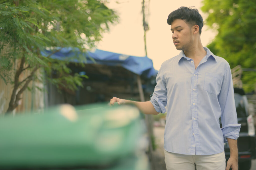 Asian man contemplates a set of bins before deciding what to throw away in each bin