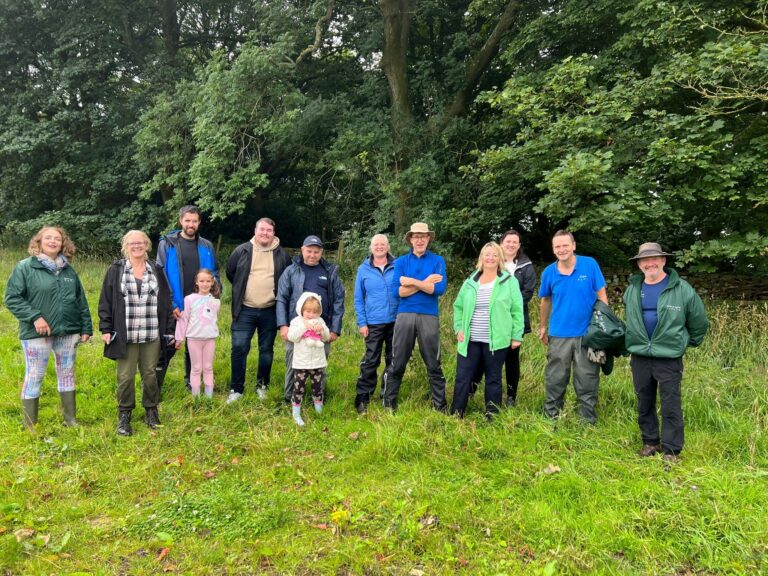 A group from We Seal volunteering with the Make it Wild organisation in North Yorkshire. The group are standing in a wild meadow surrounded by trees